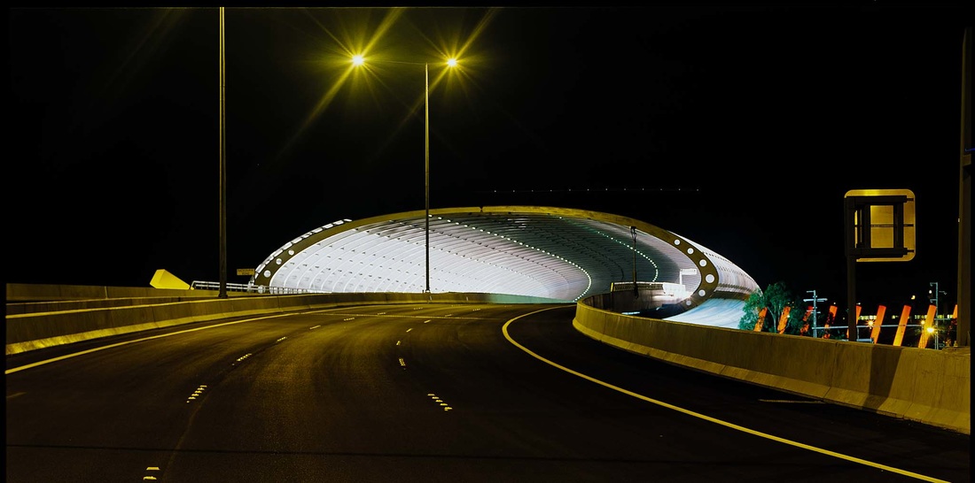 Empty freeway at night curving into the glowing ribbed vault of the CityLink sound tube, Melbourne